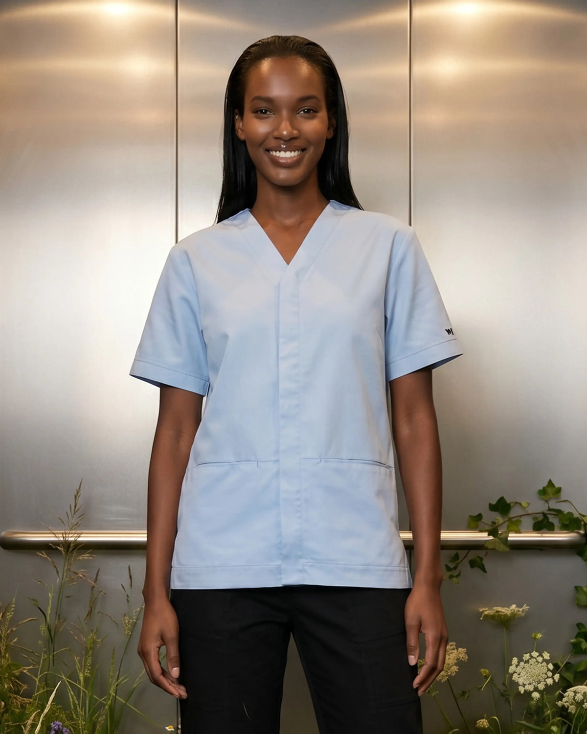 Tunique médicale Orchis bleu ciel col V, portée sur pantalon noir, coton bio - Le Vêtement Médical